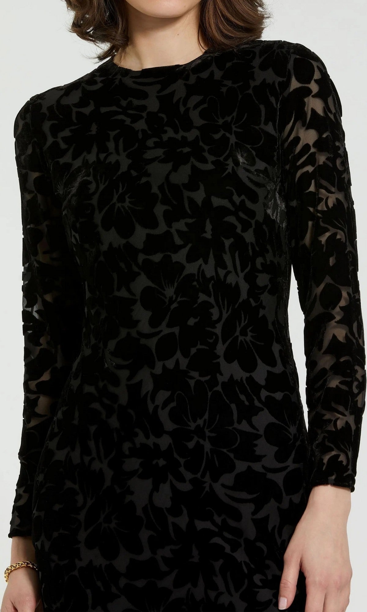 A person is wearing the Mac Duggal 81129 Midi Party Dress— a long-sleeve, black burnout velvet midi dress with a floral pattern—while standing against a plain background.